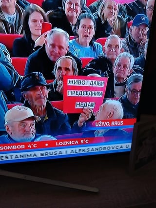 Old man in game show audience shows sign saying &amp;quot;We are all Vucic&amp;quot;